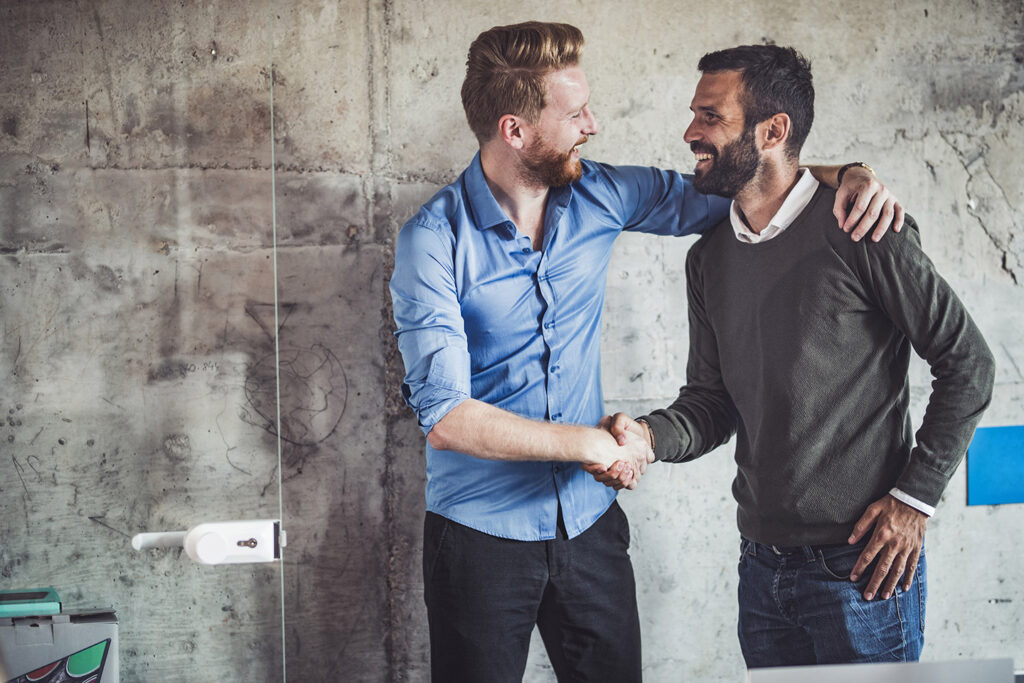 Two men shaking hands as one has hand over the other's shoulder