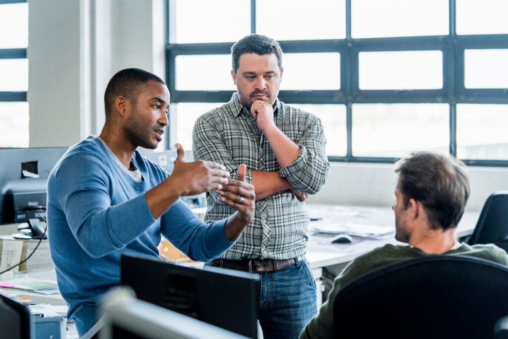 A photo of three men ideating in an open-plan workspace